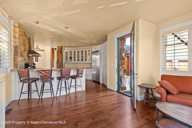 kitchen featuring wall chimney exhaust hood, dark wood-type flooring, built in refrigerator, a peninsula, and white cabinetry