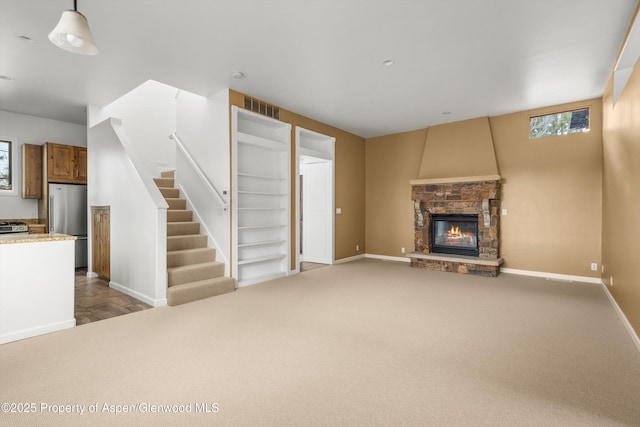 unfurnished living room with baseboards, visible vents, stairs, a stone fireplace, and dark carpet