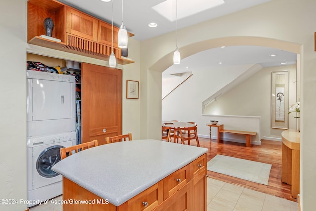 kitchen with light tile patterned floors, a kitchen island, decorative light fixtures, and stacked washer and clothes dryer