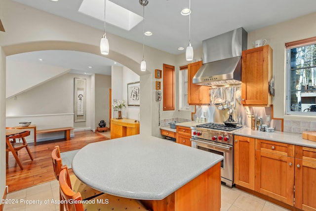 kitchen with wall chimney range hood, light tile patterned floors, premium stove, a center island, and hanging light fixtures