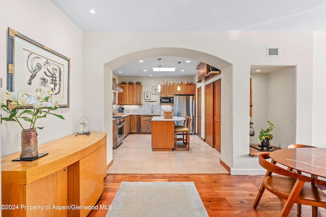 kitchen featuring a center island, backsplash, light wood-type flooring, appliances with stainless steel finishes, and a kitchen bar