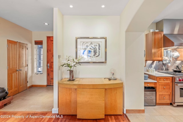 kitchen featuring stainless steel range, light tile patterned floors, backsplash, and wall chimney range hood