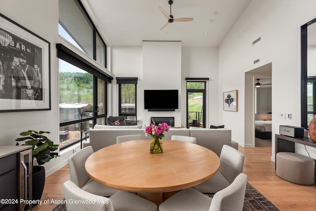 dining space with light wood-type flooring, a towering ceiling, plenty of natural light, and ceiling fan