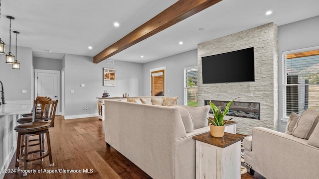 living area with beam ceiling, dark wood finished floors, recessed lighting, a stone fireplace, and baseboards