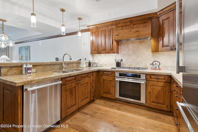 kitchen featuring sink, light hardwood / wood-style flooring, decorative light fixtures, decorative backsplash, and appliances with stainless steel finishes