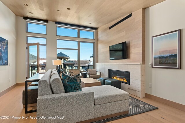 living room with a tile fireplace, wood ceiling, a high ceiling, and light hardwood / wood-style floors