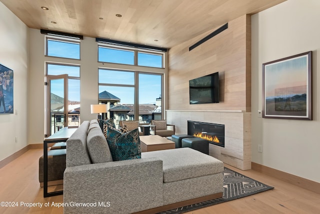 living room with a tile fireplace, wood ceiling, a high ceiling, and light hardwood / wood-style floors