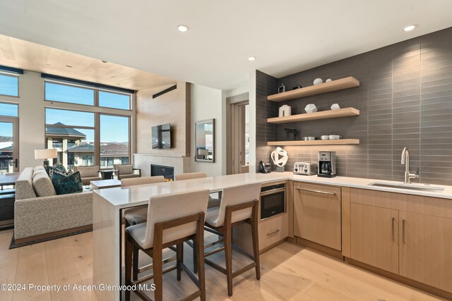 kitchen with sink, a kitchen breakfast bar, light hardwood / wood-style flooring, kitchen peninsula, and light brown cabinetry