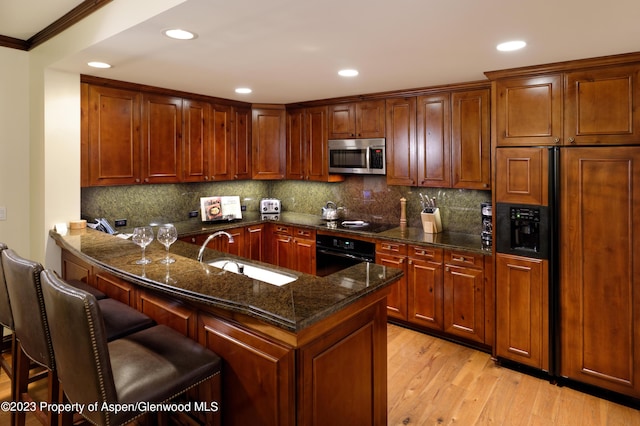 kitchen with black appliances, light hardwood / wood-style floors, sink, a kitchen breakfast bar, and crown molding