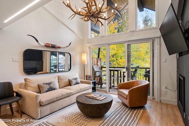 living room with plenty of natural light, high vaulted ceiling, wood-type flooring, and an inviting chandelier