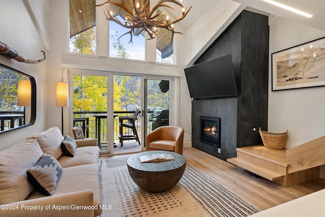 living room with a tile fireplace, an inviting chandelier, a towering ceiling, and hardwood / wood-style flooring