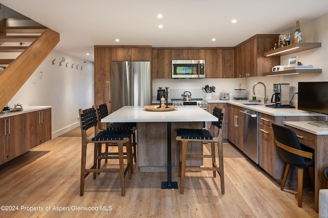 kitchen with sink, a center island, light hardwood / wood-style floors, a breakfast bar, and appliances with stainless steel finishes