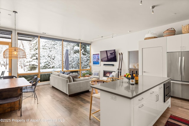 kitchen featuring an island with sink, white cabinets, stainless steel fridge, and wood-type flooring