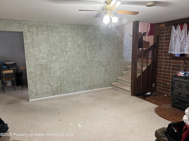 carpeted living area with baseboards, ceiling fan, stairs, and wallpapered walls