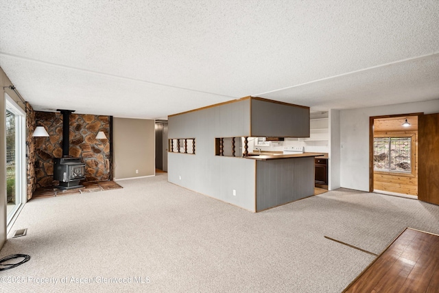 unfurnished living room featuring visible vents, a textured ceiling, light colored carpet, and a wood stove