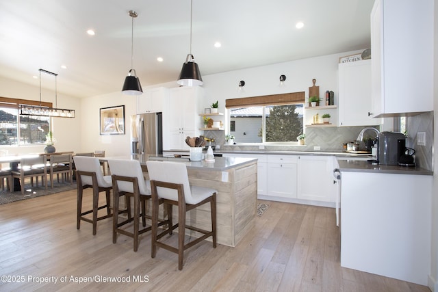 kitchen featuring a center island, stainless steel fridge, light hardwood / wood-style floors, tasteful backsplash, and white cabinetry