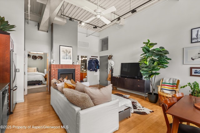 living area featuring light wood-type flooring, track lighting, a ceiling fan, a high ceiling, and a fireplace