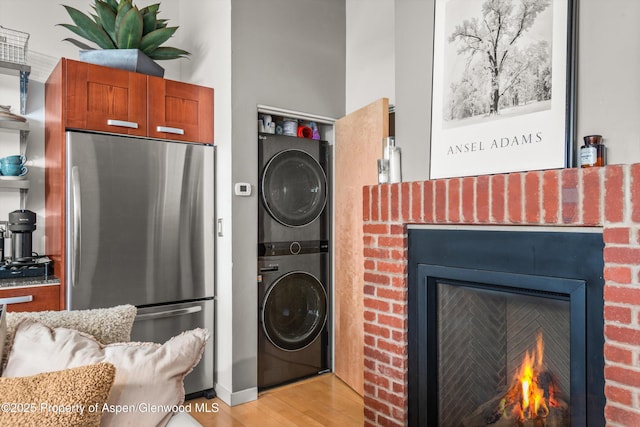 laundry room featuring laundry area, a fireplace, light wood-type flooring, and stacked washer and dryer