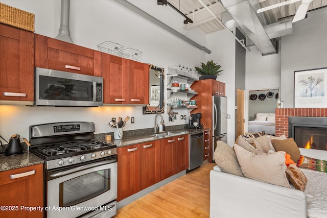 kitchen featuring light wood finished floors, open floor plan, a high ceiling, stainless steel appliances, and a sink