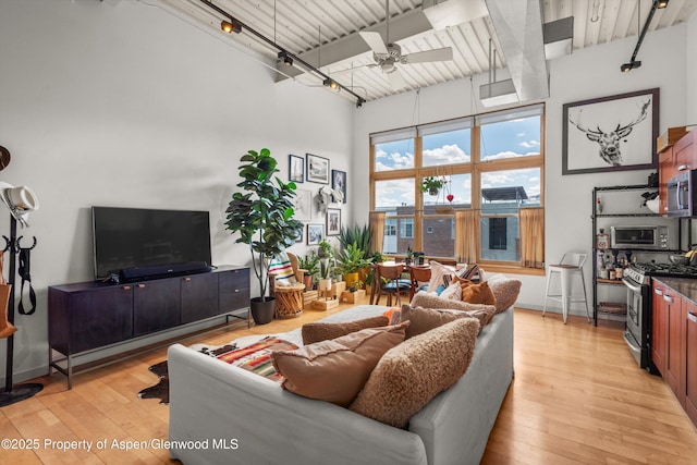 living area with light wood finished floors, beam ceiling, a high ceiling, and ceiling fan