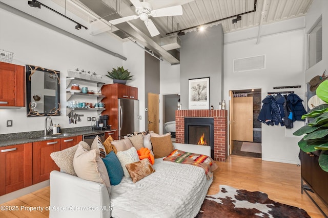 living room with visible vents, ceiling fan, a fireplace, light wood-style floors, and a towering ceiling