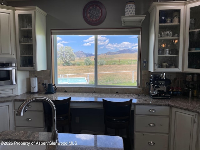 kitchen featuring oven, white cabinets, decorative backsplash, glass insert cabinets, and a mountain view