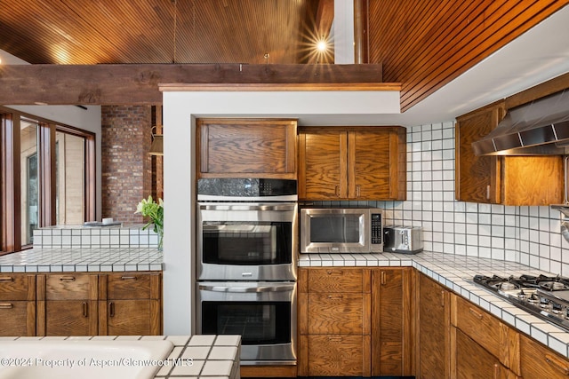 kitchen with tile counters, stainless steel appliances, wooden ceiling, extractor fan, and decorative backsplash