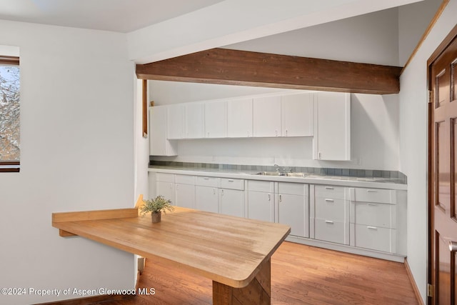 kitchen featuring beam ceiling, sink, white cabinets, and light hardwood / wood-style floors