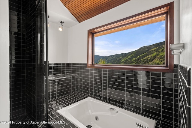 bathroom with a mountain view, vaulted ceiling, wooden ceiling, and tiled tub