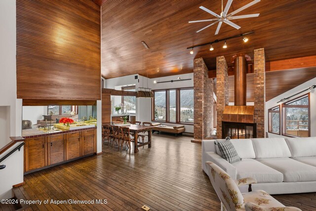 living room featuring ceiling fan, dark wood-type flooring, wooden ceiling, a multi sided fireplace, and a high ceiling