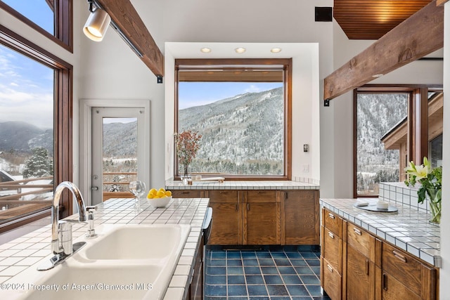 kitchen featuring beam ceiling, sink, tile countertops, a mountain view, and plenty of natural light