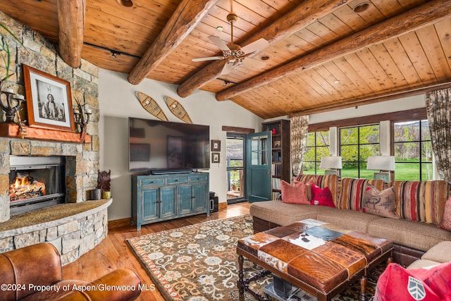 living room featuring beam ceiling, ceiling fan, a stone fireplace, light hardwood / wood-style flooring, and wood ceiling