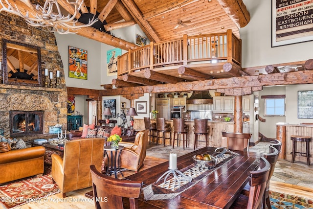 dining area featuring beam ceiling, a fireplace, high vaulted ceiling, and ceiling fan with notable chandelier