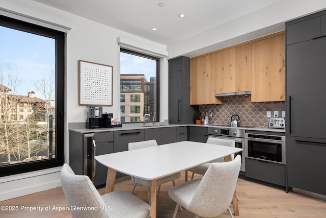 kitchen featuring stainless steel oven, gray cabinets, oven, light hardwood / wood-style floors, and backsplash