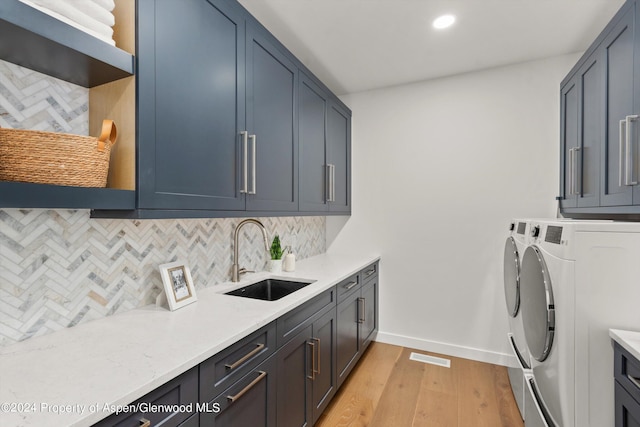 laundry area featuring cabinets, light hardwood / wood-style floors, washer and clothes dryer, and sink