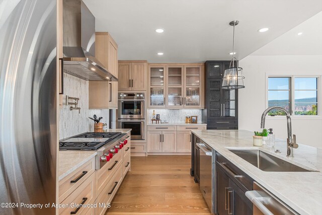 kitchen with pendant lighting, wall chimney range hood, sink, appliances with stainless steel finishes, and tasteful backsplash