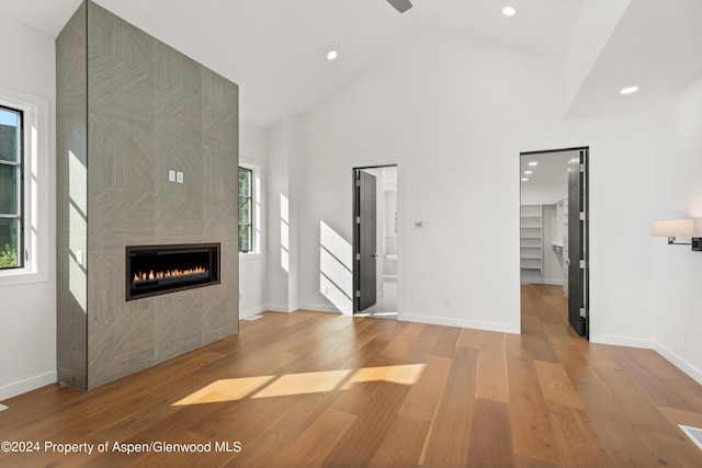 unfurnished living room with a tiled fireplace, high vaulted ceiling, and light wood-type flooring