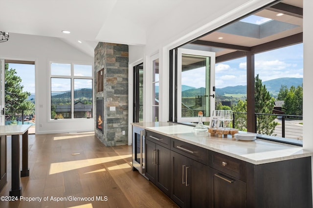 interior space with light stone countertops, vaulted ceiling with skylight, dark brown cabinetry, a mountain view, and hardwood / wood-style floors