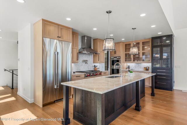 kitchen with light stone countertops, backsplash, wall chimney exhaust hood, stainless steel appliances, and a center island with sink