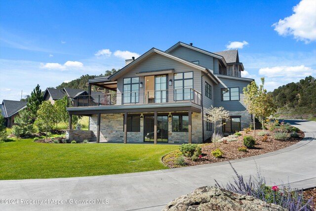 rear view of property featuring a balcony and a lawn