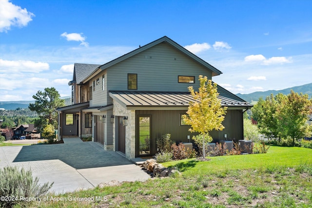 rear view of property with a mountain view, a yard, a garage, and central AC unit