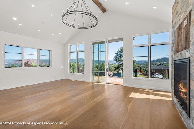 unfurnished living room with a mountain view, an inviting chandelier, beamed ceiling, light hardwood / wood-style floors, and a stone fireplace