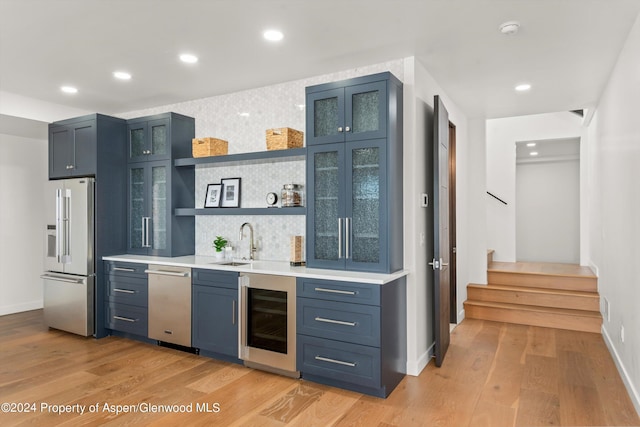 bar featuring beverage cooler, stainless steel appliances, tasteful backsplash, light hardwood / wood-style flooring, and blue cabinets