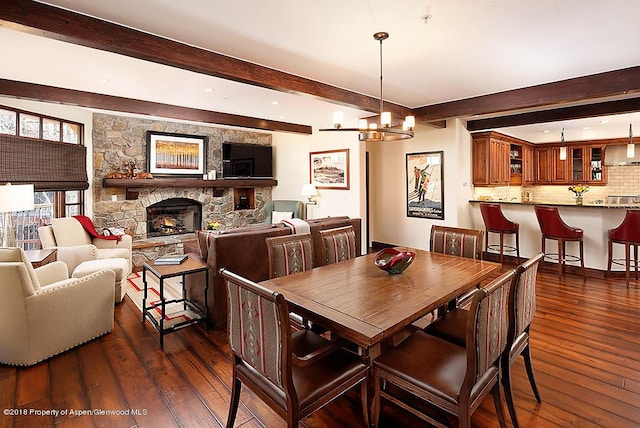 dining room with beamed ceiling, a stone fireplace, an inviting chandelier, and dark hardwood / wood-style flooring