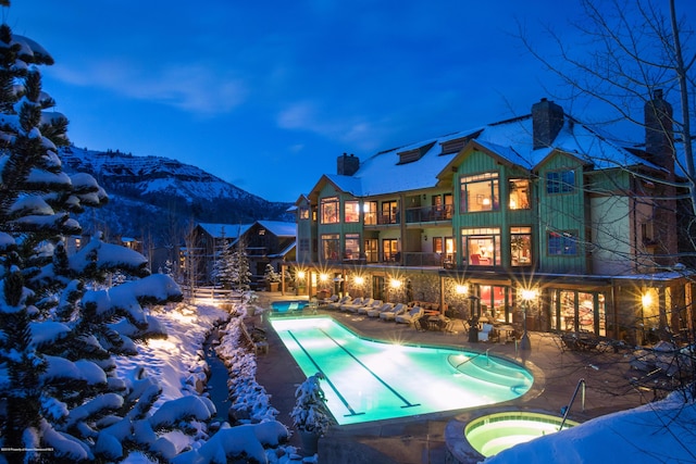 snow covered pool with a mountain view, a patio, and an in ground hot tub