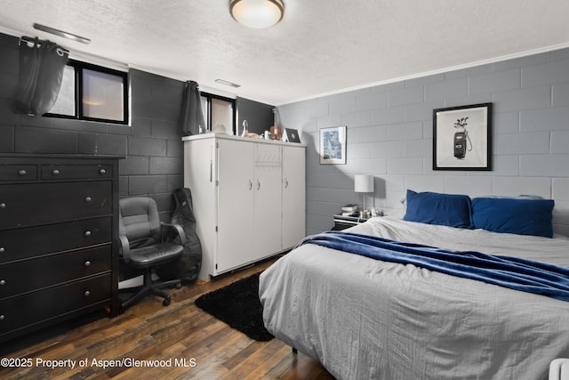 bedroom with a textured ceiling, dark wood-style flooring, and concrete block wall