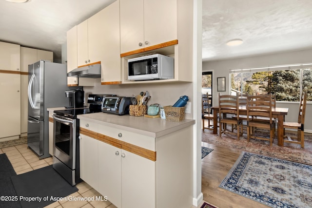 kitchen with light tile patterned floors, a toaster, under cabinet range hood, light countertops, and appliances with stainless steel finishes