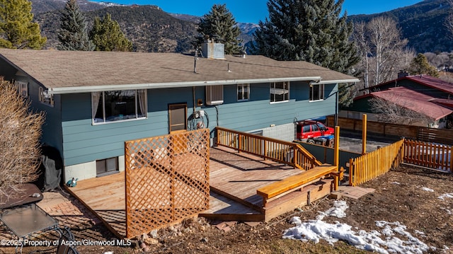 rear view of house featuring a deck with mountain view, a chimney, and fence