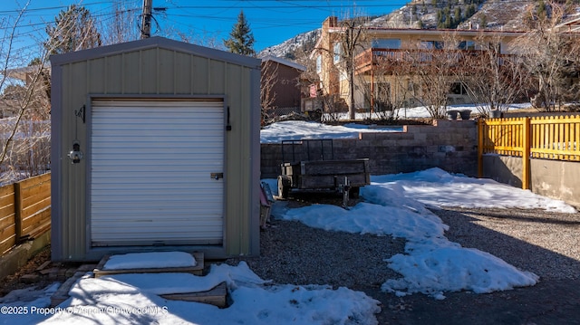 snow covered structure with an outbuilding, a storage unit, and a fenced backyard