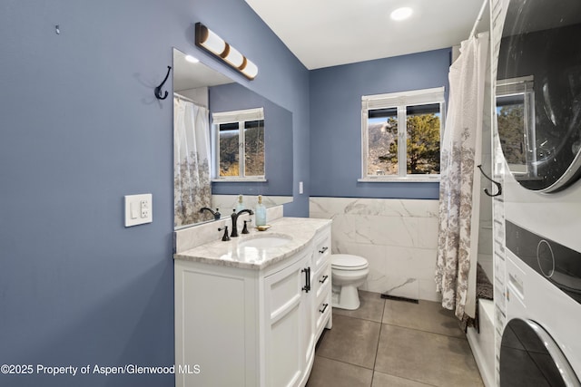 full bathroom with toilet, tile walls, vanity, stacked washer / drying machine, and tile patterned floors